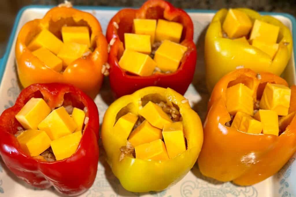 Colorful bell peppers in baking pan stuffed with cheese and other fillings.