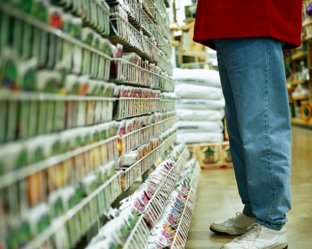 Man standing in garden center aisle, looking at dozens of racks of seed packets.
