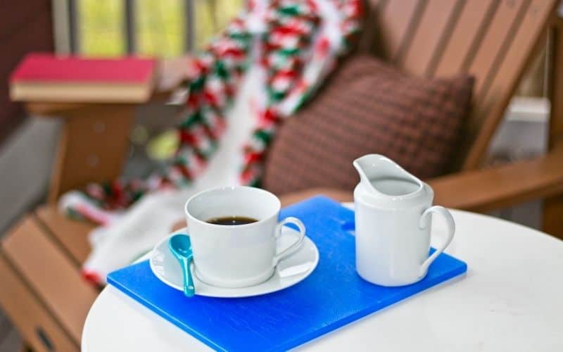 A blue tray with a coffee cup sitting on a saucer and creamer in a white dish, sitting on a table on a porch outside.