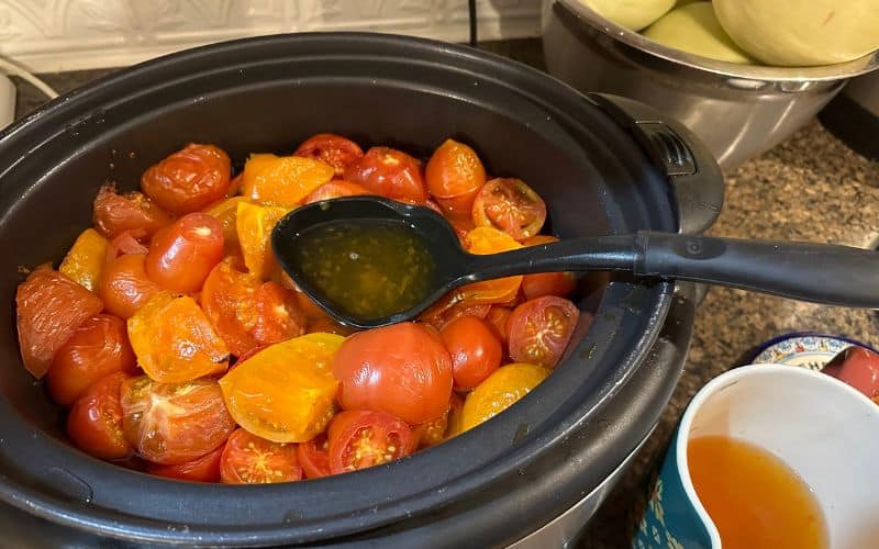 Using ladle to remove excess liquid from tomatoes cooking in a slow cooker.