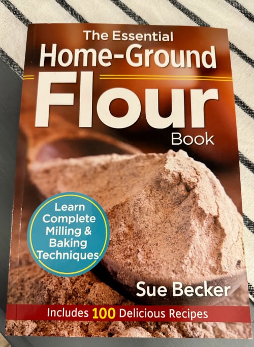 Copy of The Essential Home Ground Flour Book by Sue Becker on a striped table runner.