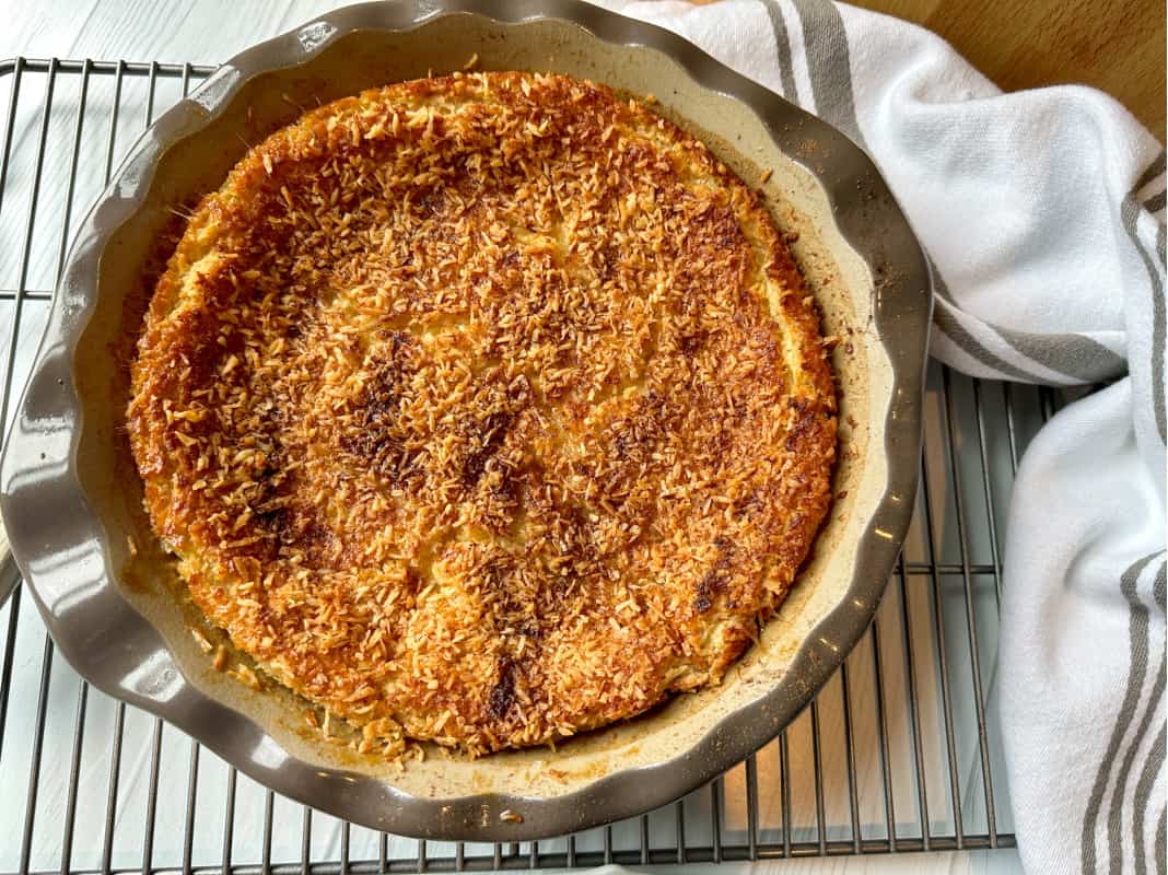 Finished Impossible Coconut Custard Pie in a grey stoneware pie dish on a cooling rack
