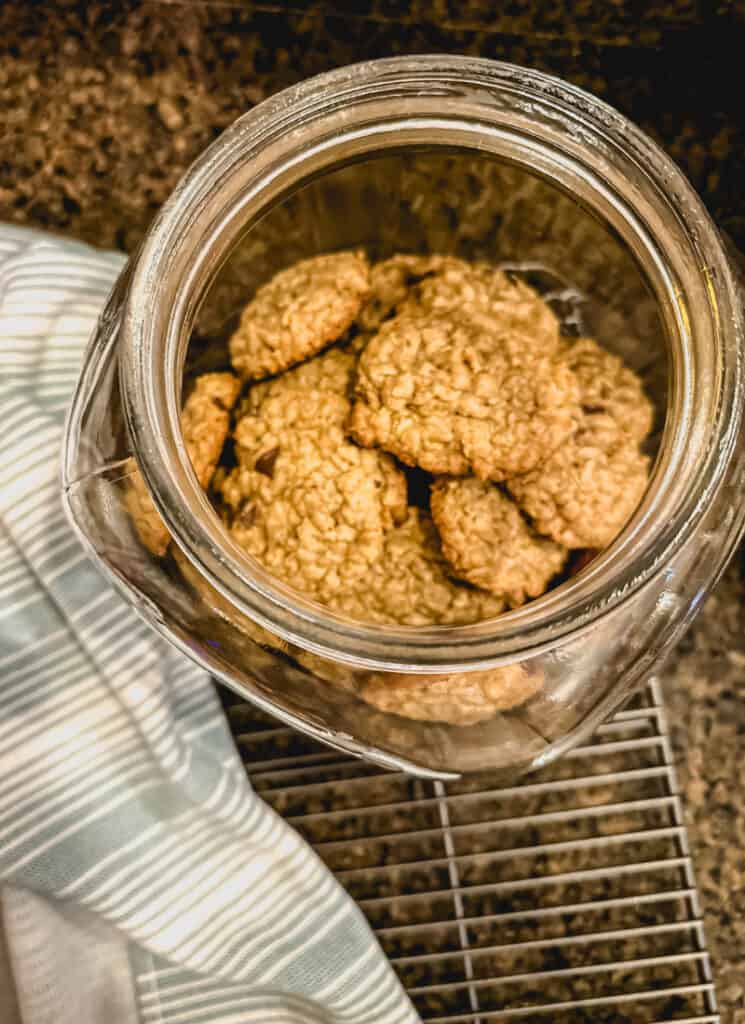 Looking into a large glass canister filled with Oatmeal spelt cookies with chocolate chips. 