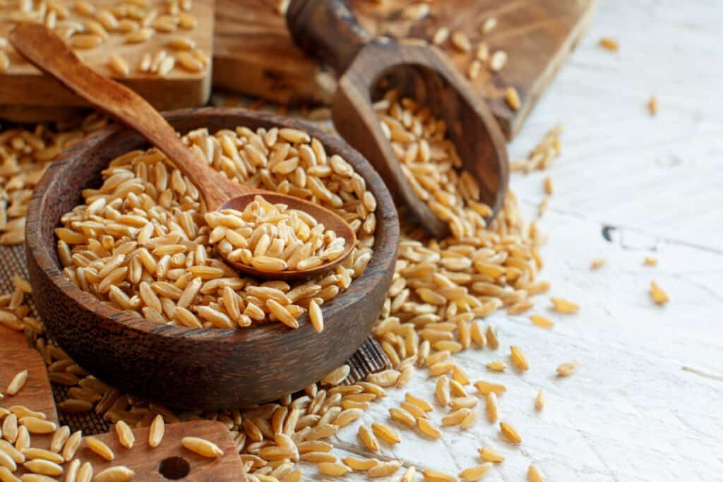 wheat berries in a wooden bowl and wooden scoop on a white table.