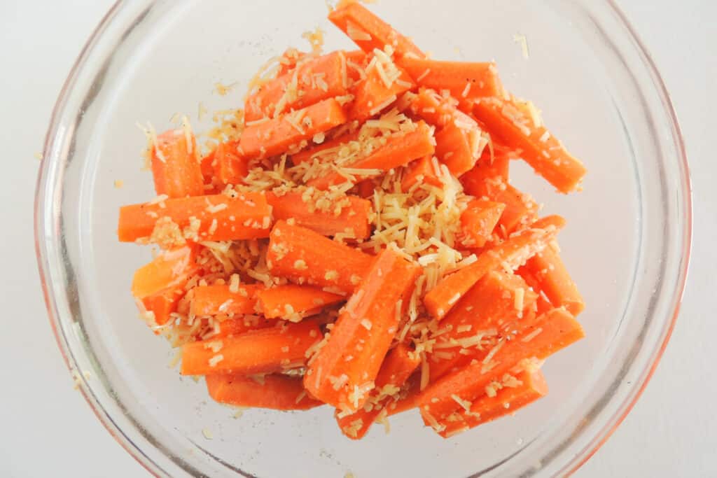 Tossing the carrot sticks in cheeses, olive oil and garlic in a glass bowl.