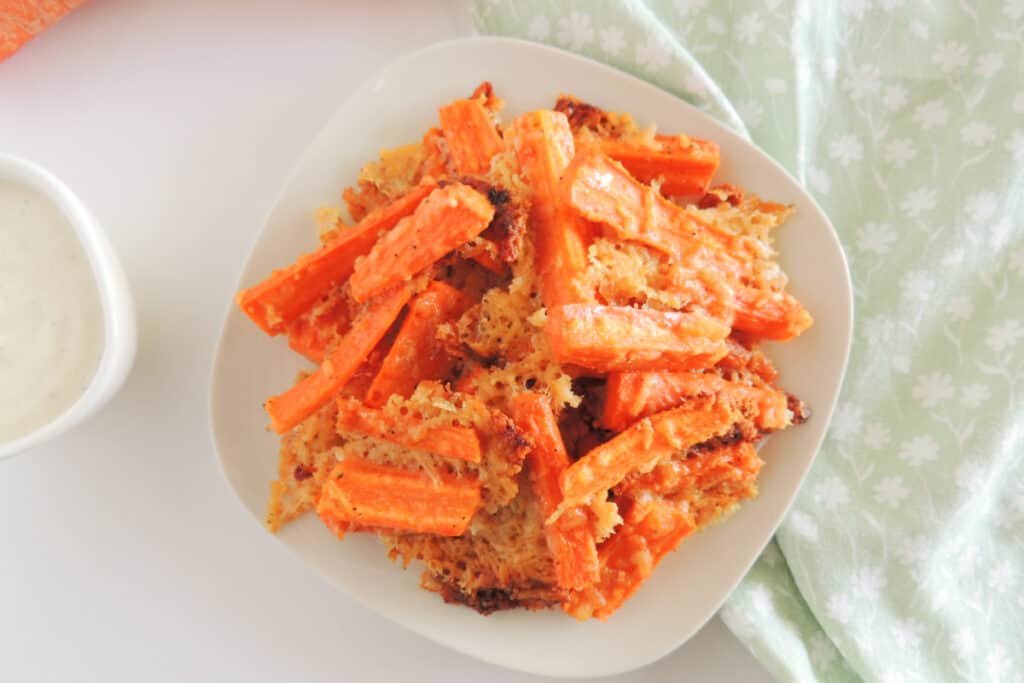 Roasted parmesan carrot sticks in a white bowl on a light colored tablescape.