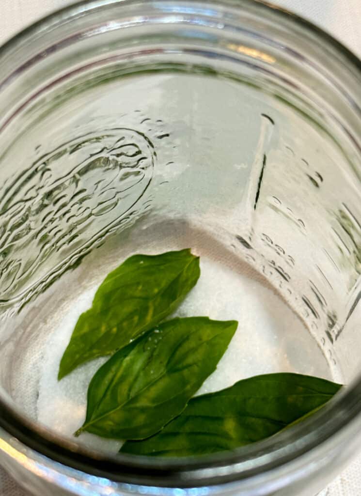Placing first layer of basil on salt in a mason jar.