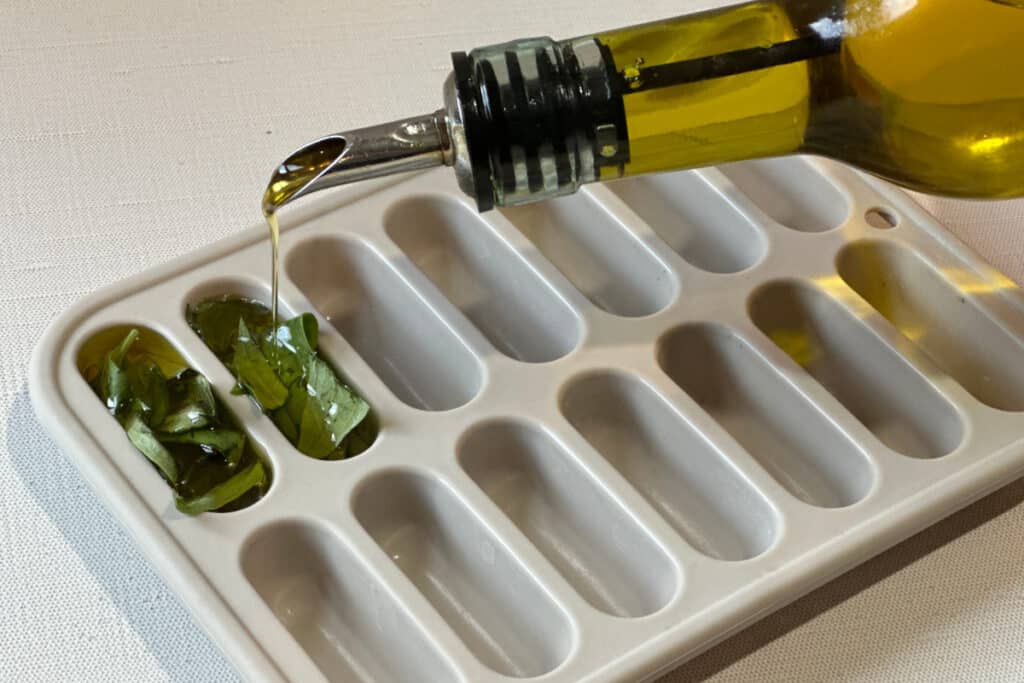 Pouring olive oil over strips of basil in a silicone ice cube tray.