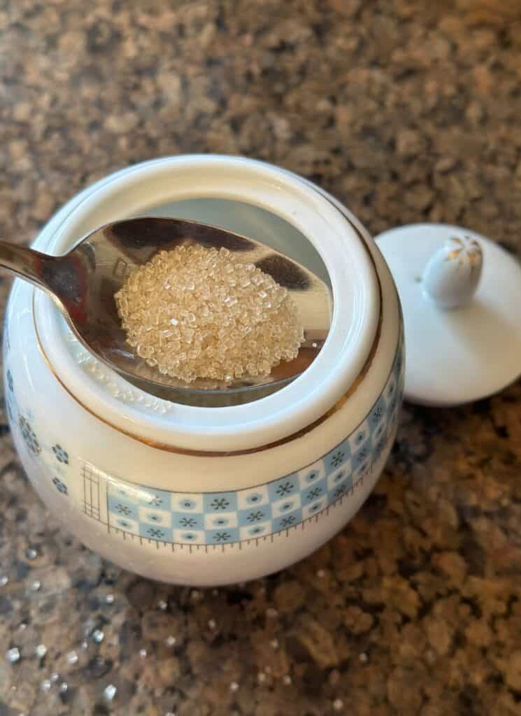 Organic cane sugar being spooned out of a small sugar bowl.