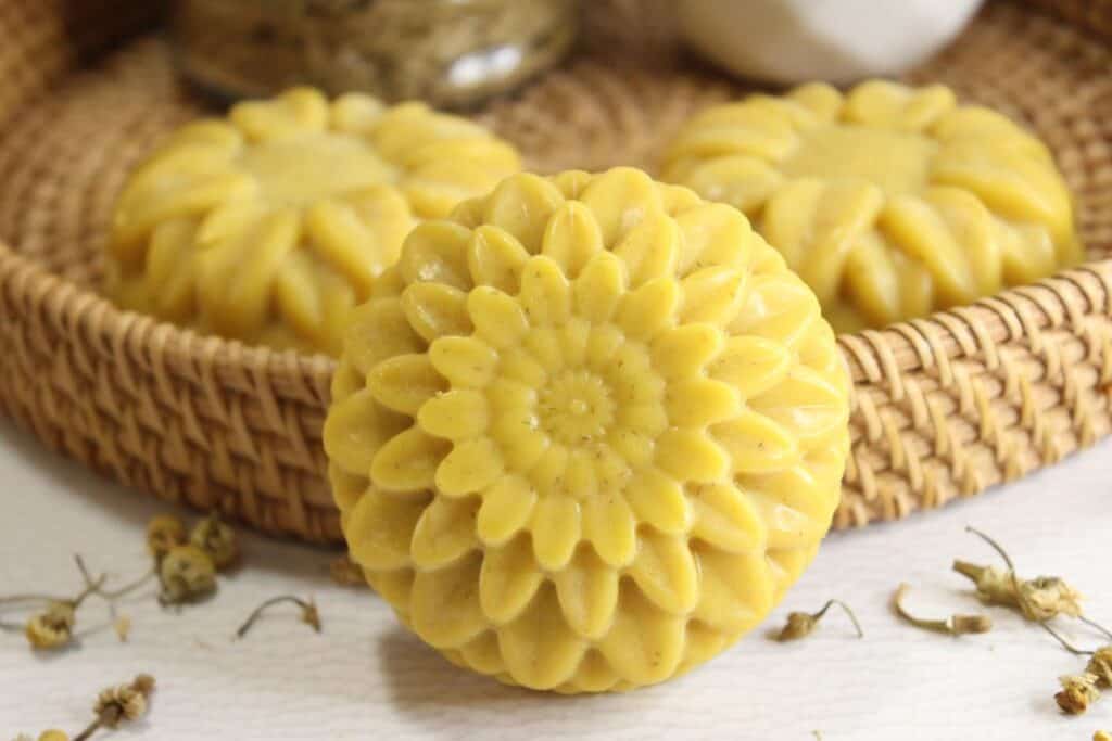 Close up of bar of chamomile soap in a flower shape against a background with more soaps.