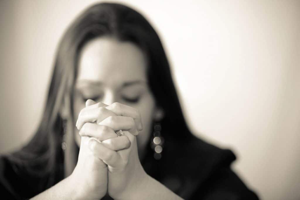 Black and white photo of young woman praying with hands folded.