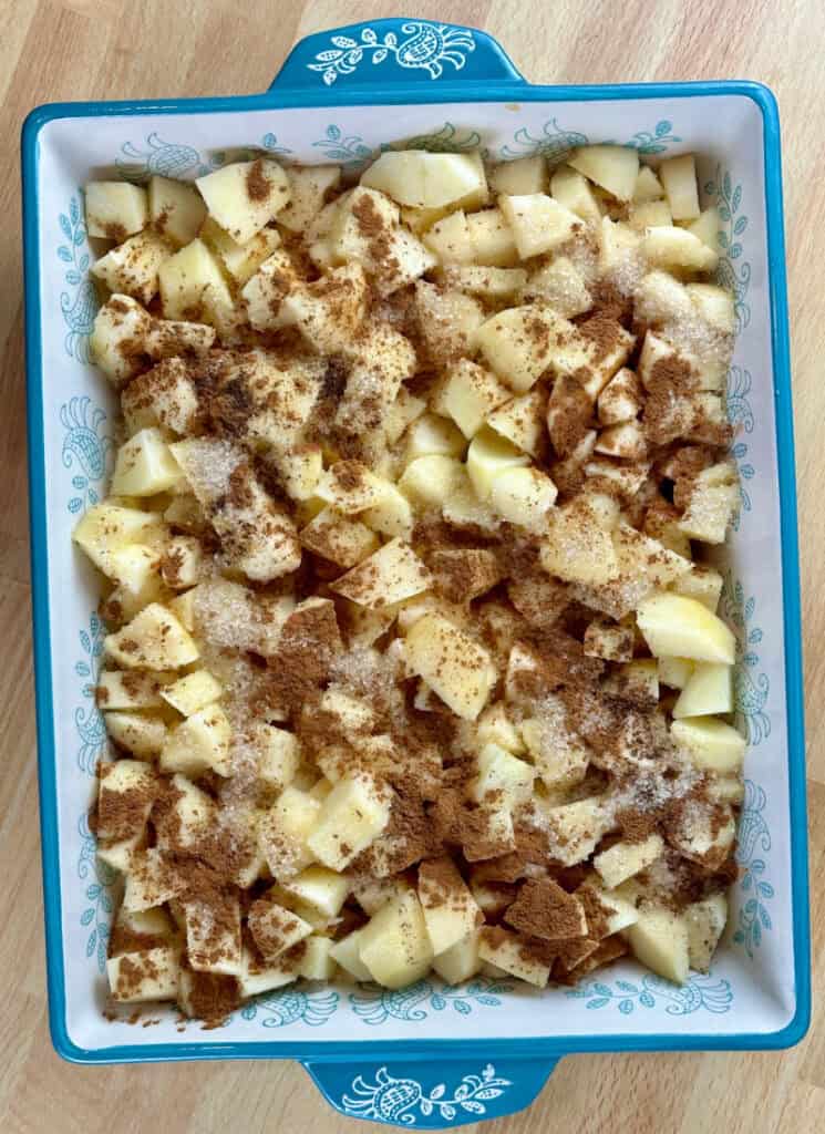 Apple cobbler filling: diced apples in a large baking dish sprinkled with cinnamon and sugar.