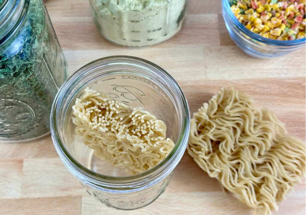 Ramen in a mason jar with dry ingredients on wooden table.