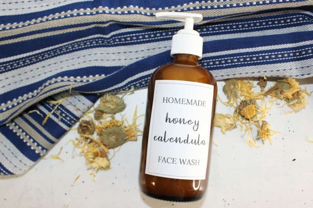 honey calendula face wash on white background with dried flowers and blue tea towel.