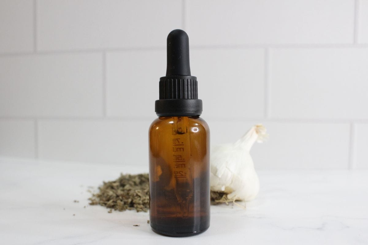 Glass dropper bottle with ear oil and mullein and garlic in background.