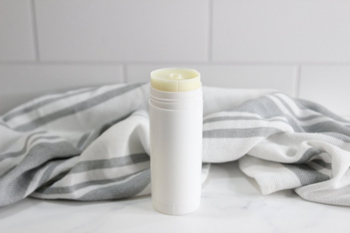 Sunscreen stick on white surface with grey striped towel in background.