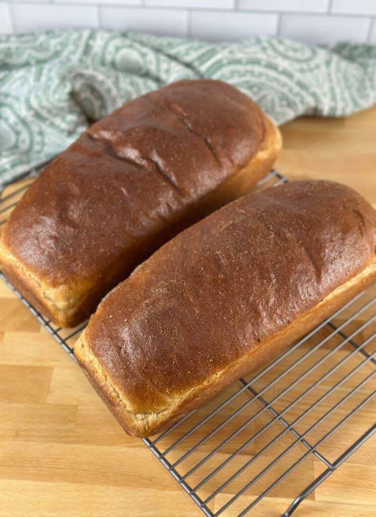Two fresh milled loaves of sandwich bread on cooling rack.