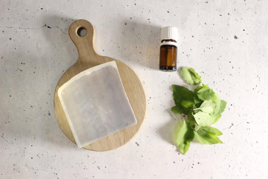 Glycerin soap on cutting board with jewelweed leaves and bottle of essential oils next to it.
