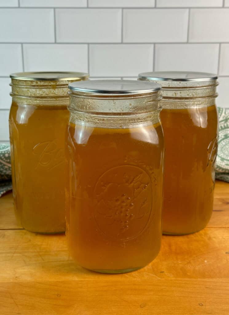 Three jars of homemade chicken stock on wooden table.
