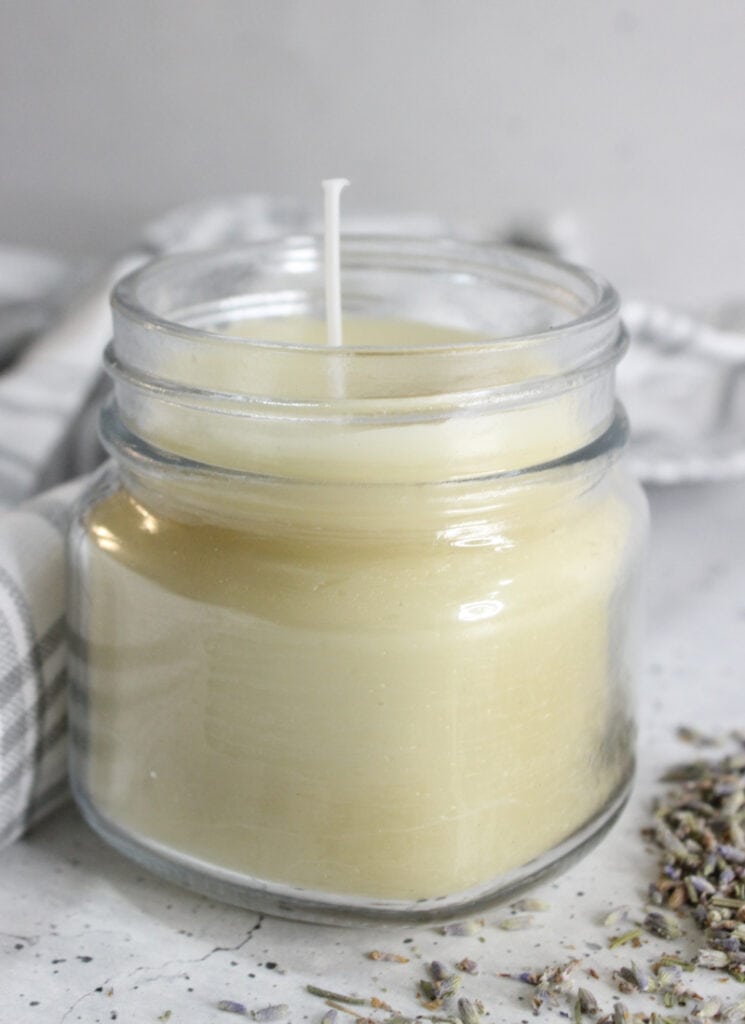 Lavender infused candle in a glass jar with lavender petals and tea towel nearby.