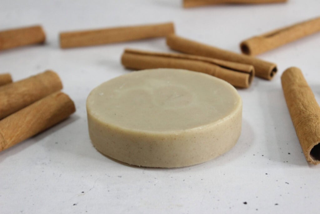 Round lotion bars with cinnamon sticks on speckled countertop.
