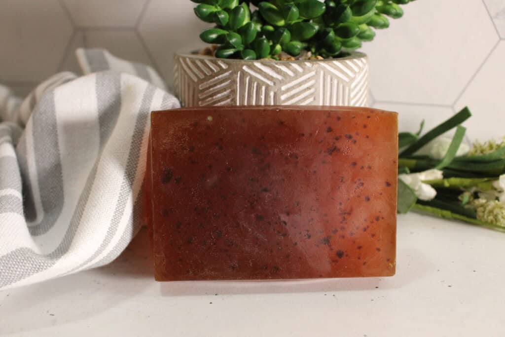 tumeric soap bar standing up on countertop with green plant in background.