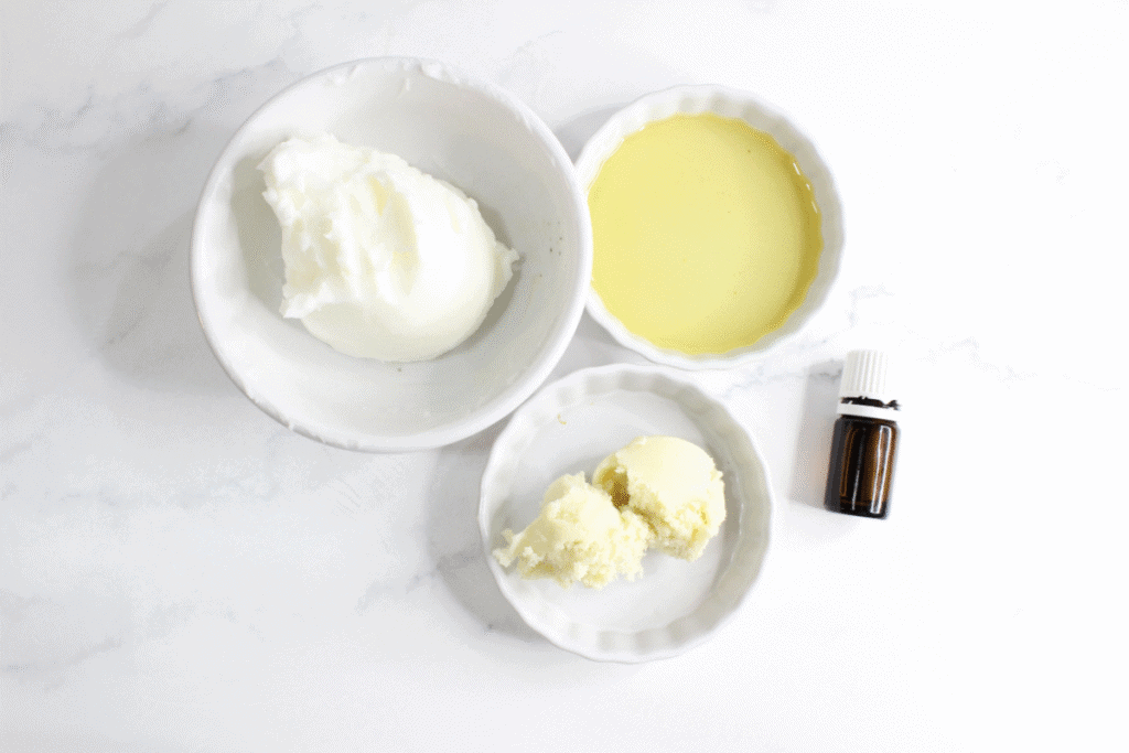 Ingredients for tallow lotion measured out in small ceramic bowls with a bottle of essential oils next to them.