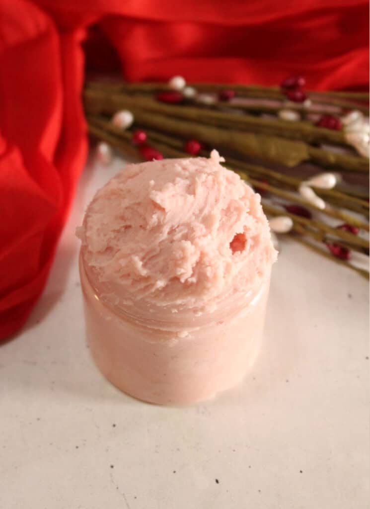 Vertical image of whipped pink colored body butter in small jar.