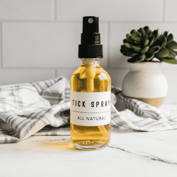 Small bottle of homemade tick spray on marble countertop with towel and plant in background.