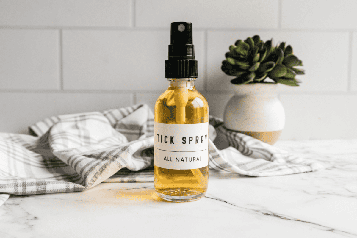 Small bottle of homemade tick spray on marble countertop with towel and plant in background.