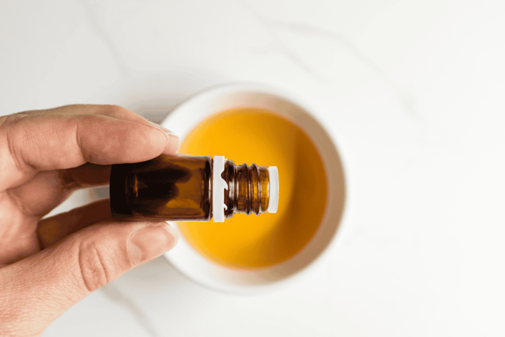 Holding a bottle of essential oils to drop oil into the ACV mixture.